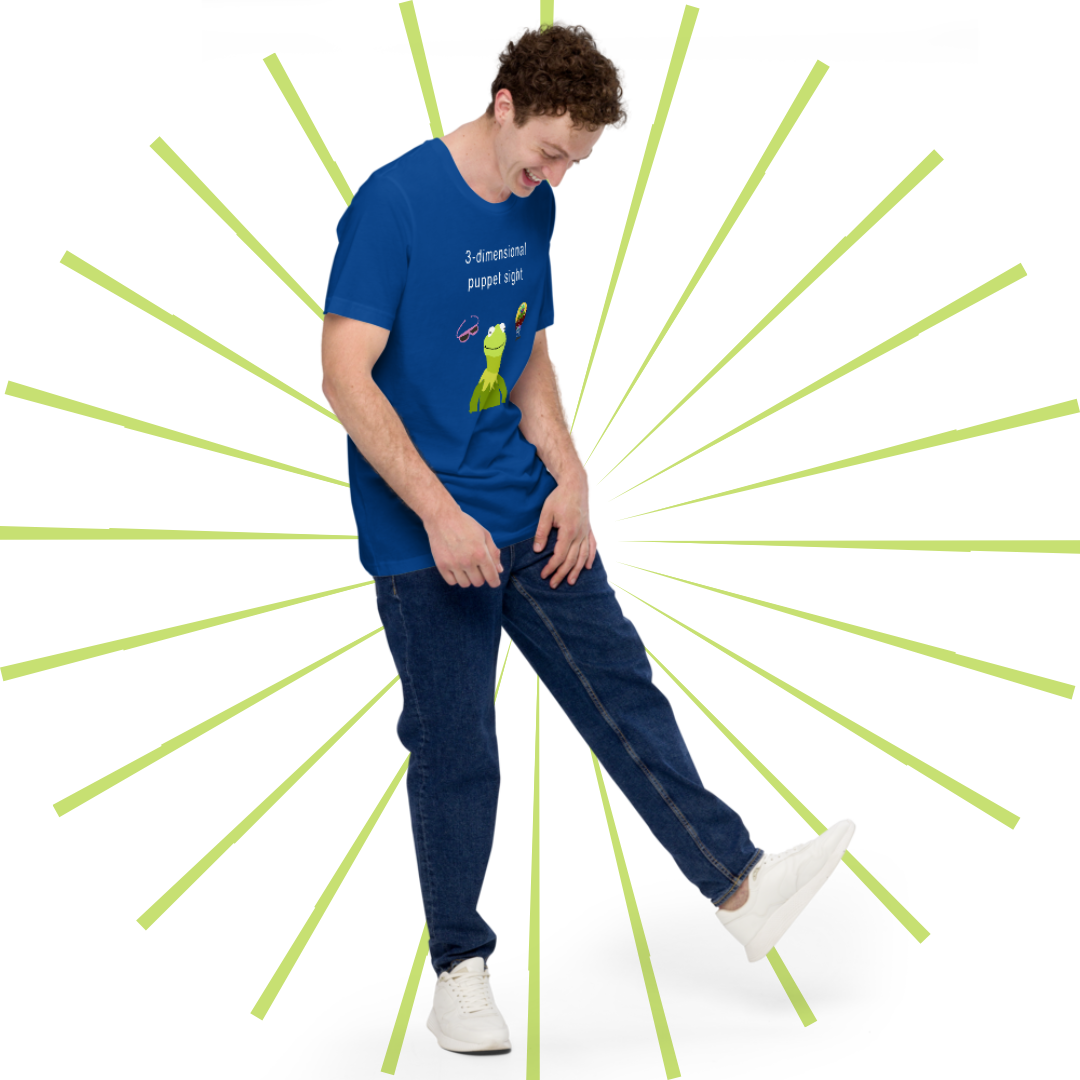 Young, average-sized Caucasian man with curly hair wearing the blue version of the T-shirt paired with a pair of jeans and white sneakers. He smiles as he gazes down, kicking his left foot out playfully.