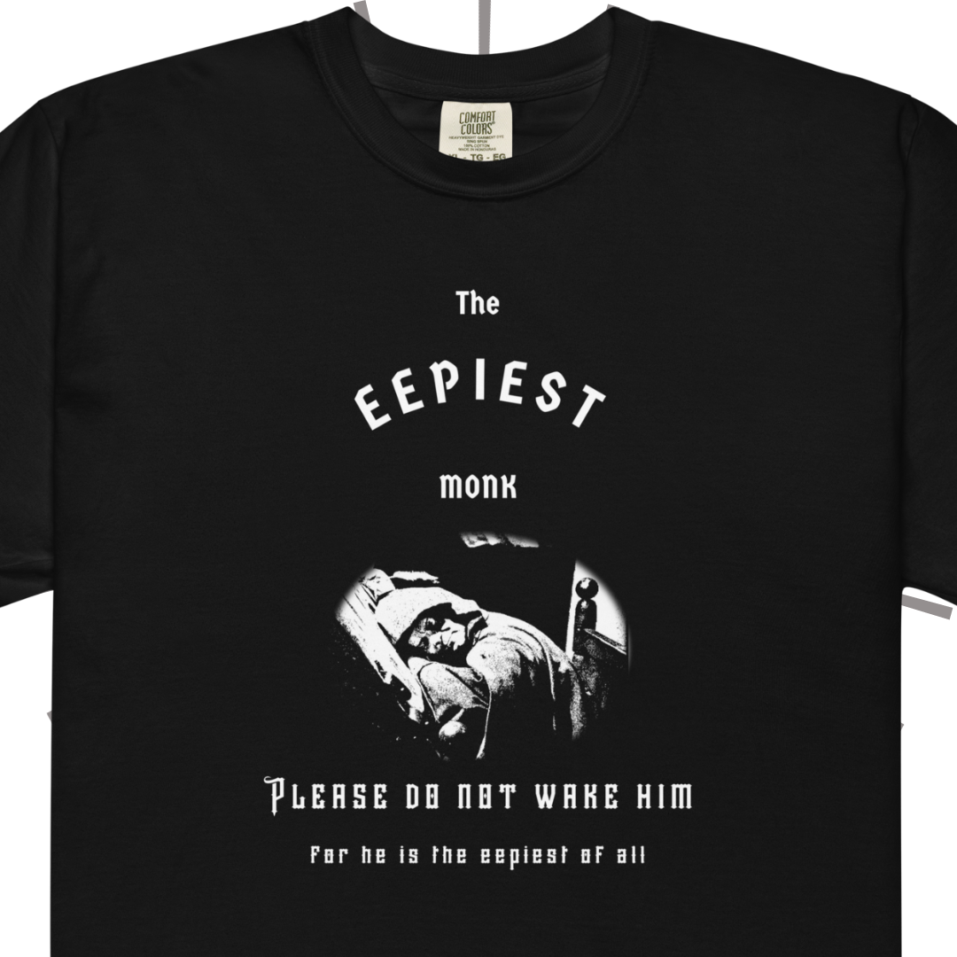 A closer shot of The Eepiest Monk tee. Front side of a black T-shirt with medieval-inspired white text reading "The Eepiest Monk" at the top. Below that is a rendering of the sleeping monk animatronic from the Spaceship Earth ride at Epcot in Disney World, all in white. Below that is more medieval-inspired text reading "Please do not wake him for he is the eepiest of all."