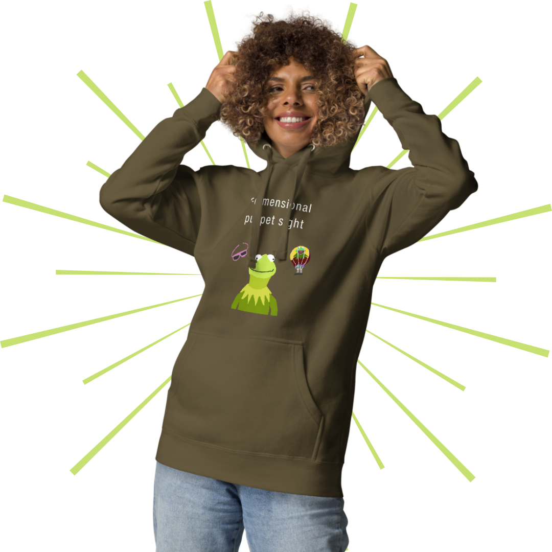 Average-sized woman of color with curly, light brown hair wearing the camouflage green version of the hoodie. She smiles as she pulls the hood up over her head, smiling off towards her left side.