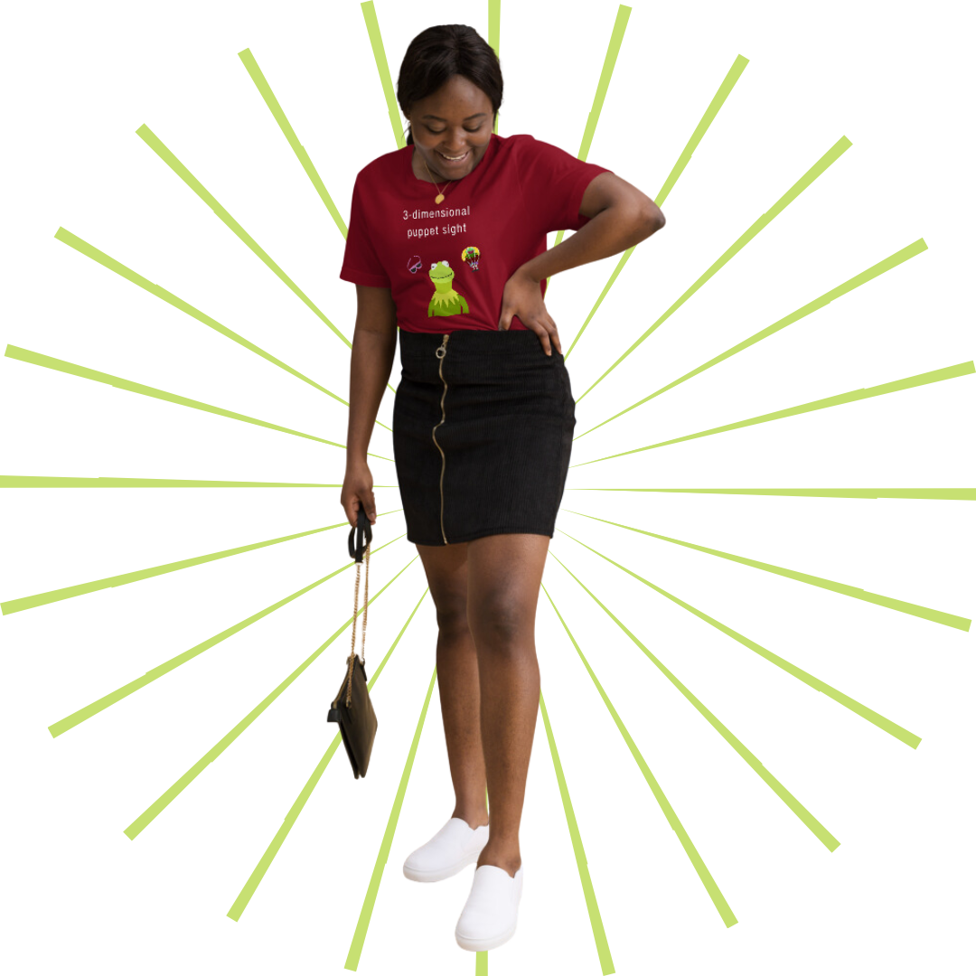 Young, average-sized Black woman wearing the red version of the T-shirt tucked into a short, black zippered pencil skirt and pair of white, slip-on sneakers. She is standing with her left hand on her hip and a purse in her right. She gazes down at her feet as she smiles.